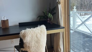Una habitación con un escritorio de madera, un sillón mullido, una planta en maceta y vistas a una terraza nevada a través de una ventana.