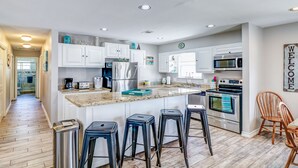 Une cuisine moderne avec des meubles blancs, des appareils en acier inoxydable et un îlot central doté de tabourets de bar.