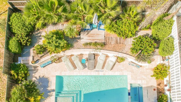 Vue aérienne d’un complexe hôtelier doté d’une grande piscine, de chaises longues et de palmiers.