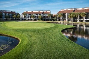 Een goed onderhouden golfbaan met een vijver, omringd door meerlaagsgebouwen met balkons.