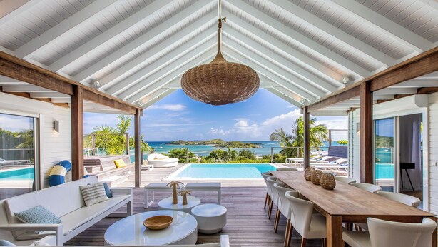 A covered outdoor area with a wooden deck, white furniture, and a view of a swimming pool and ocean. - A dream villa for an unforgettable holiday! (SAINT MARTIN)