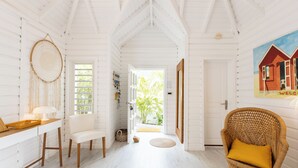 A bright, white interior with a high ceiling, a wicker chair with a yellow cushion, and a painting of a house on the wall. - A dream villa for an unforgettable holiday! (SAINT MARTIN)