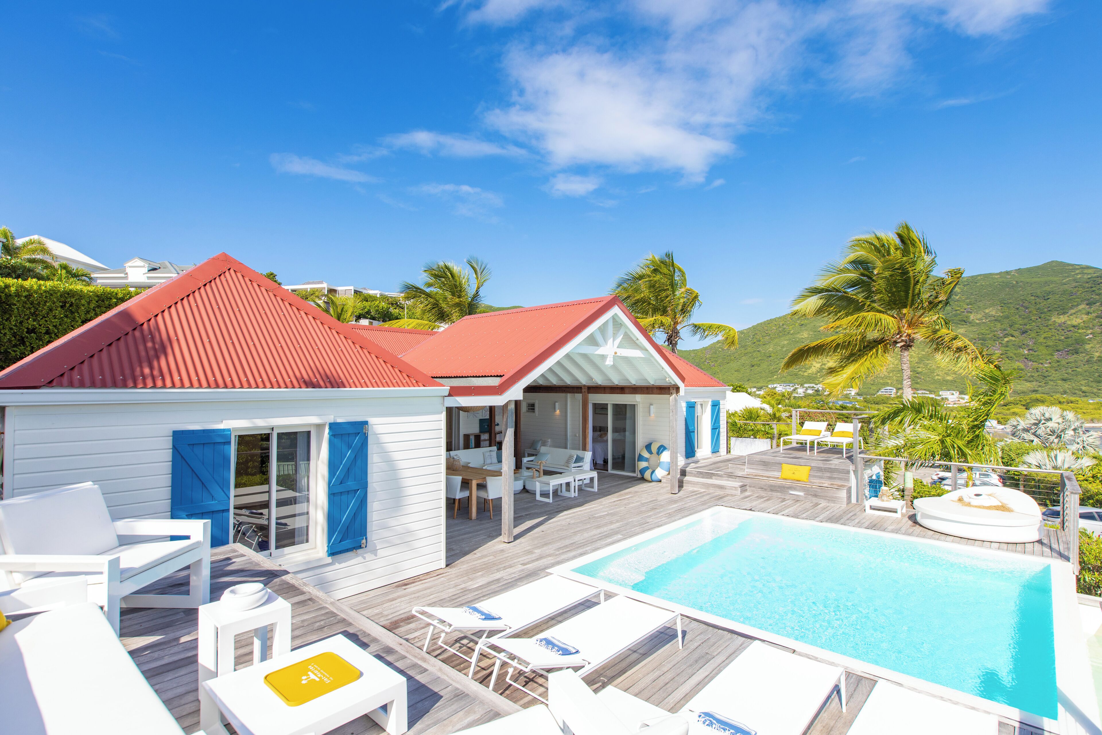 Un espace aménagé au bord de la piscine, avec une terrasse en bois, des chaises longues blanches et une piscine.