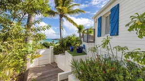 A wooden deck leading to a white house with blue shutters, surrounded by tropical plants and a view of the ocean. - A dream villa for an unforgettable holiday! (SAINT MARTIN)