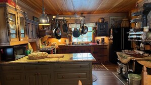 Una cocina rústica con armarios de madera, una isla central, ollas colgantes y una estufa antigua.