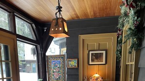 Una habitación acogedora con techo de madera, un ventanal grande, un banco de madera, una mesita con una vela y una lámpara de pared.
