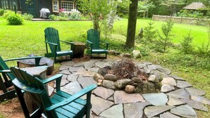 Un hogar de piedra rodeado de sillas Adirondack verdes en un jardín.