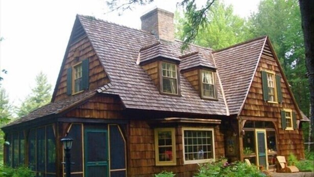 Una casa de madera con techo inclinado, ventanas grandes y una chimenea visible.