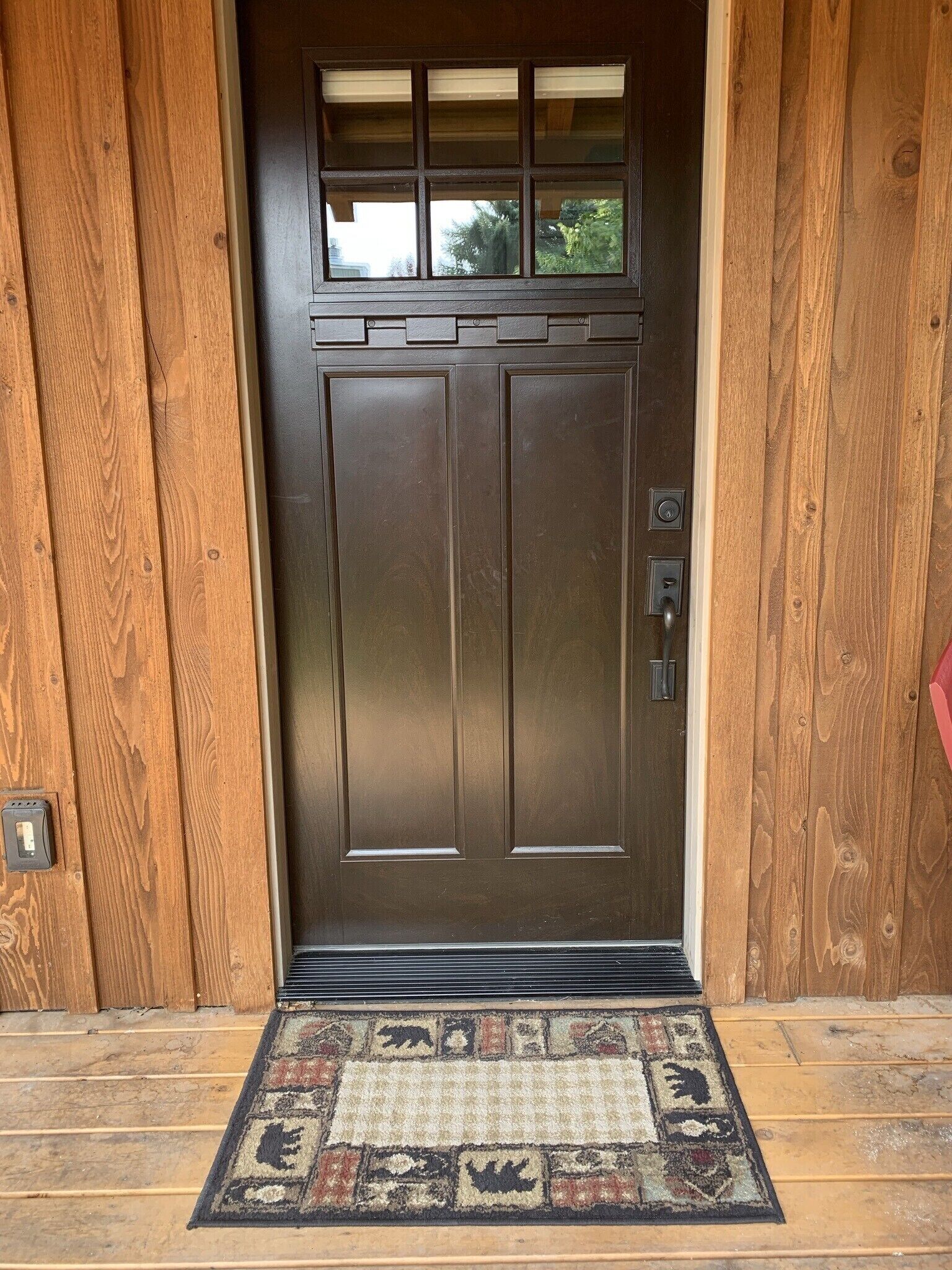 A wooden door with a window above it, a doormat with animal prints, and a doorbell.