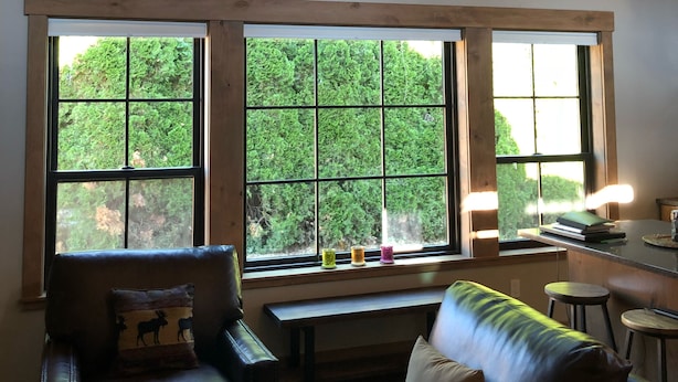 A cozy living room with a large wooden ceiling, a wall clock, and large windows overlooking greenery.