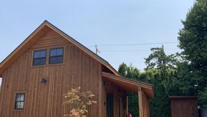A wooden cabin with a porch, a small tree, and a shed in the backyard.