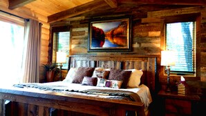 Un dormitorio rústico de madera con una cama grande, un cuadro sobre la cabecera y una ventana con persianas.
