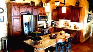 Una cocina con armarios de madera, electrodomésticos de acero inoxidable, encimera de granito y una isla central con sillas.