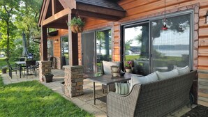Un patio techado con mobiliario exterior, una parrilla y vistas a un lago.