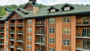 A multi-story hotel with balconies, a stone chimney, and a green roof. - 2BR with Great Mountain views Master Suite and JR suite (Gatlinburg)