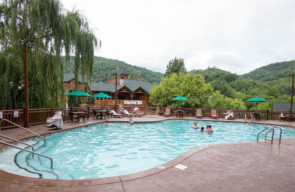 A swimming pool with lounge chairs and umbrellas, surrounded by a wooden deck and a building with a green roof.