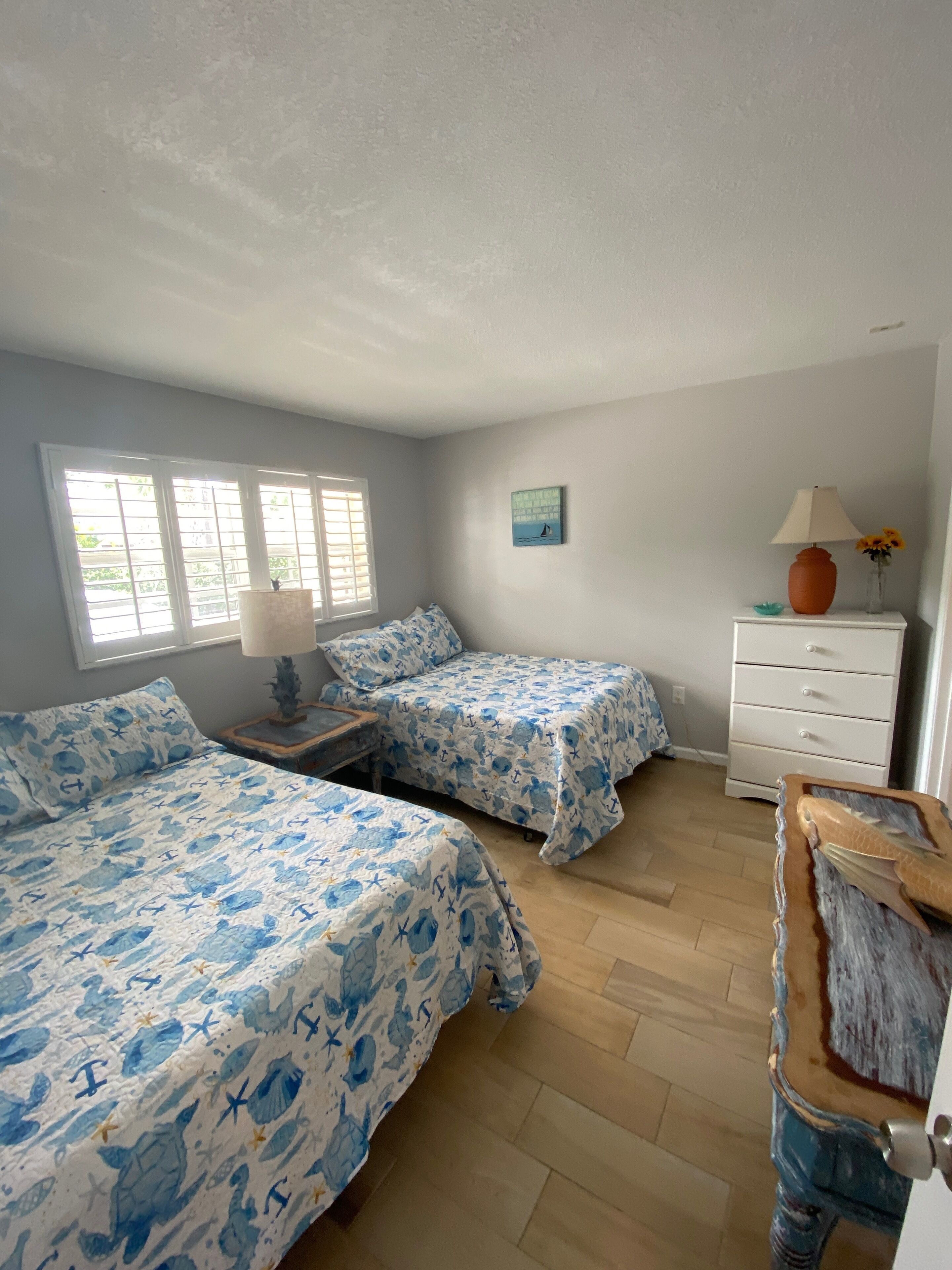 A room with two beds, a dresser, a lamp, and a painting on the wall.