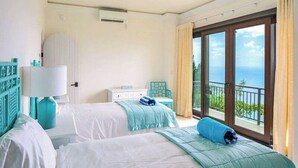 Een hotelkamer met twee bedden, een raam met uitzicht op de oceaan en een balkon met een hekwerk.