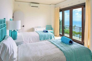 Ein Hotelzimmer mit zwei Betten, einem Fenster mit Meerblick und einem Balkon mit Geländer.