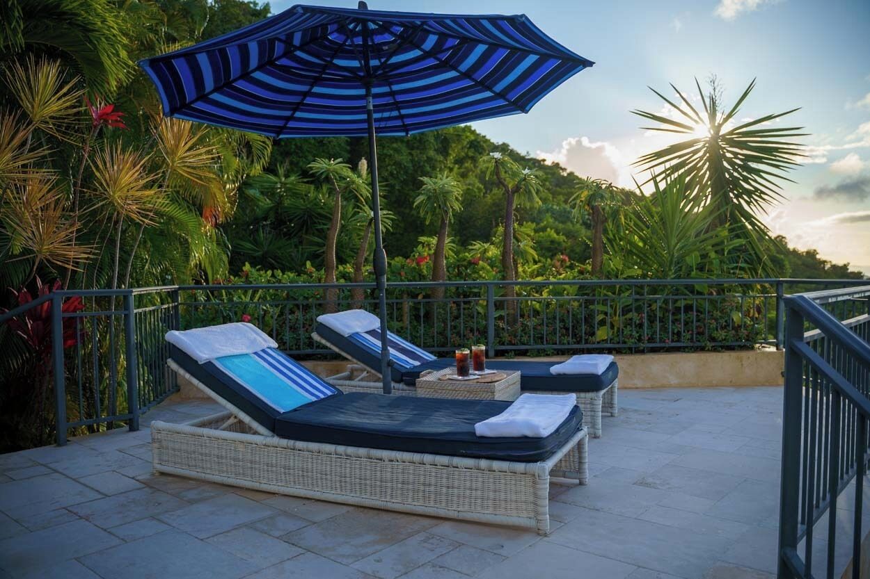 Zona relaxant a la terrassa amb seients de vimet, un parasol rayat i vista a la vegetació tropical.