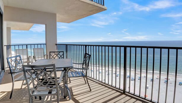 A balcony with a table and chairs overlooking a beach.