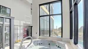 A modern indoor hot tub with a glass railing, large windows, and a view of the outside.