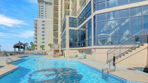 A swimming pool with clear blue water, surrounded by a multi-story building with balconies and large windows.
