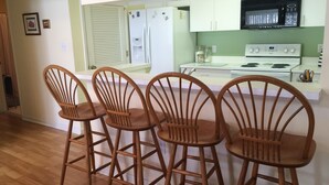 A kitchen with four wooden bar stools, a refrigerator, a microwave, a stove, and a water dispenser. - A family friendly beach retreat! (Ocean View)