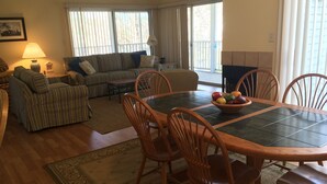 A living room with a sofa, a dining table with chairs, and a window with blinds. - A family friendly beach retreat! (Ocean View)