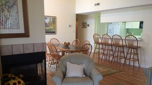 A living room with a fireplace, a dining area with a table and chairs, and a kitchen visible through an open door. - A family friendly beach retreat! (Ocean View)