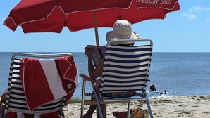 Two beach chairs with red and white striped towels, a red umbrella with "Bethany Beach" written on it, and a person sitting under the umbrella. - A family friendly beach retreat! (Ocean View)