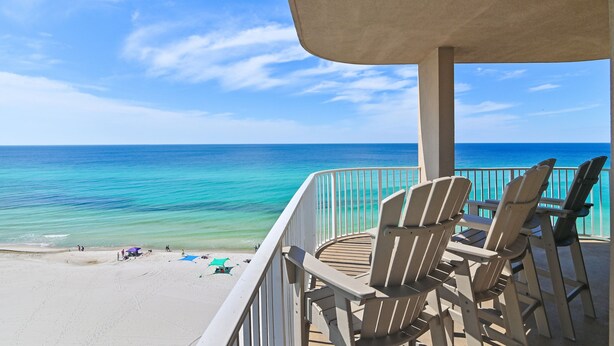 A beach view from a balcony with Adirondack chairs and a covered area.