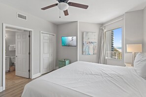 Une chambre d’hôtel équipée d’un lit, d’un ventilateur de plafond, d’une télévision, d’une fenêtre donnant sur un paysage agréable et d’une porte menant à la salle de bain.