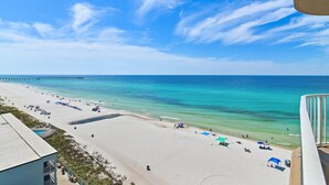 A beach with a pier extending into the ocean, clear skies, and a few umbrellas and beach chairs.