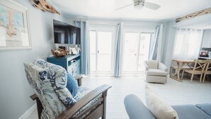 Ein geräumiges Wohnzimmer mit einer hölzernen Bank, einem Sofa, einem Fernseher auf einem Schrank und einem Essbereich mit Tisch und Stühlen.