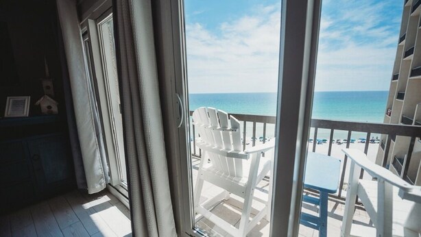 Ein Balkon mit weißen Stühlen mit Blick auf einen Strand.