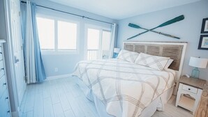 Ein Schlafzimmer mit einem Bett, einem Nachttisch, einem Fenster mit Vorhängen und einem an der Wand befestigten Surfbrett.