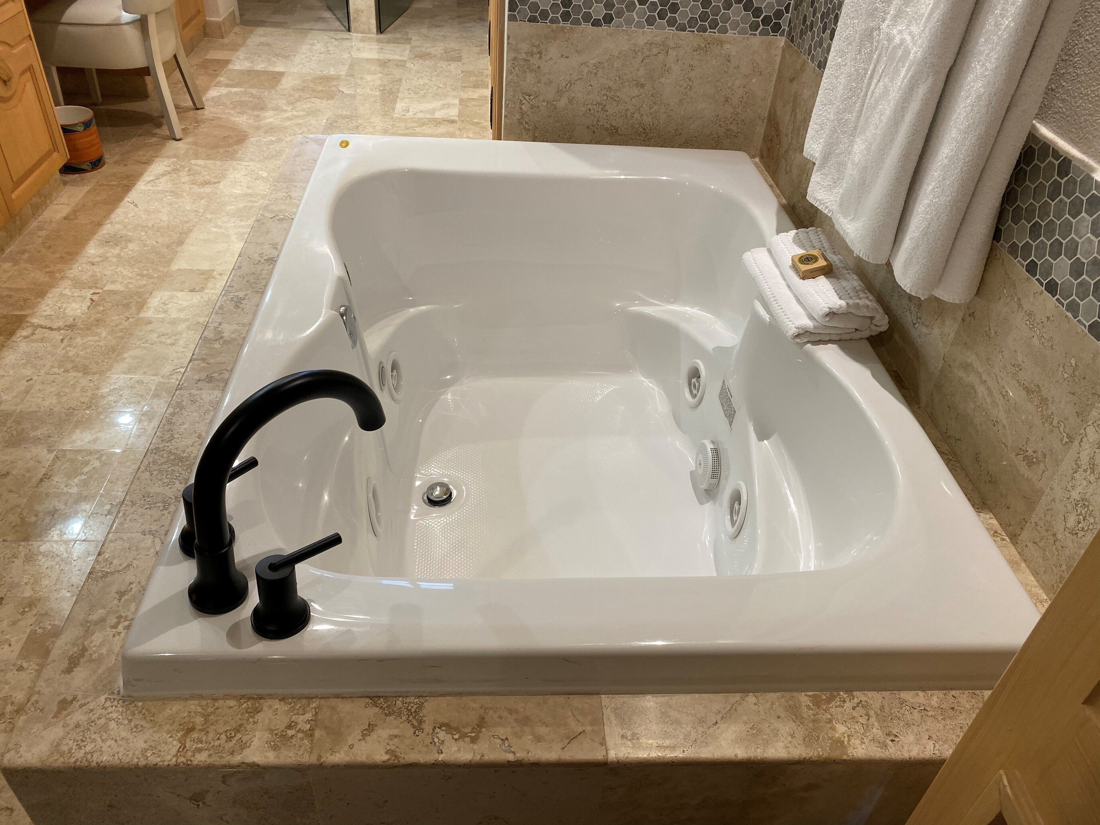 A modern bathroom with a large rectangular bathtub, a black faucet, and a tiled floor.