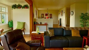 Ein Wohnzimmer mit einer Couch, einem Couchtisch und einem Esstisch mit Stühlen. Pflanzen stehen auf Regalen und eine Chandelier ist angebracht.
