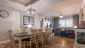 A dining area with a wooden table and chairs, a chandelier, and a view of the ocean through large windows. - Ocean Ritz 4 Bedroom 4 Bath**2 King Size beds*2 Masters on water!! (Panama City Beach)