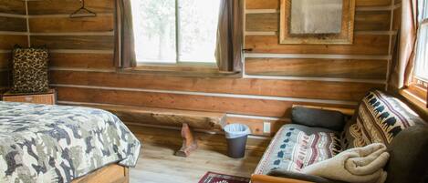 A log cabin room with a bed, a sofa, a window, and a rug.