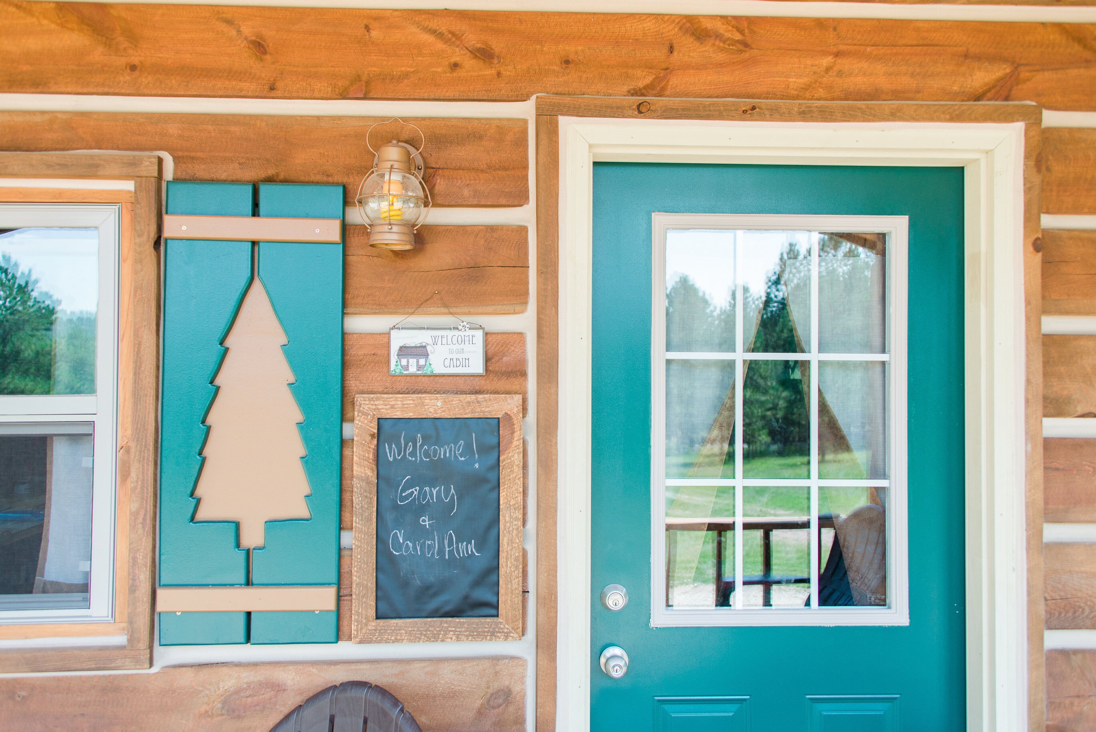 Une cabane en bois avec une porte turquoise, une pancarte de bienvenue et une décoration de Noël.