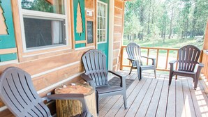 A wooden deck with Adirondack chairs and a table, overlooking a forested area.