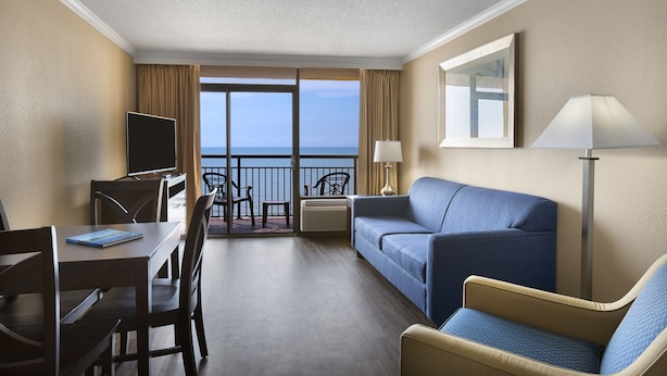 Une chambre d’hôtel avec un balcon, un canapé, un fauteuil, un bureau et une télévision.