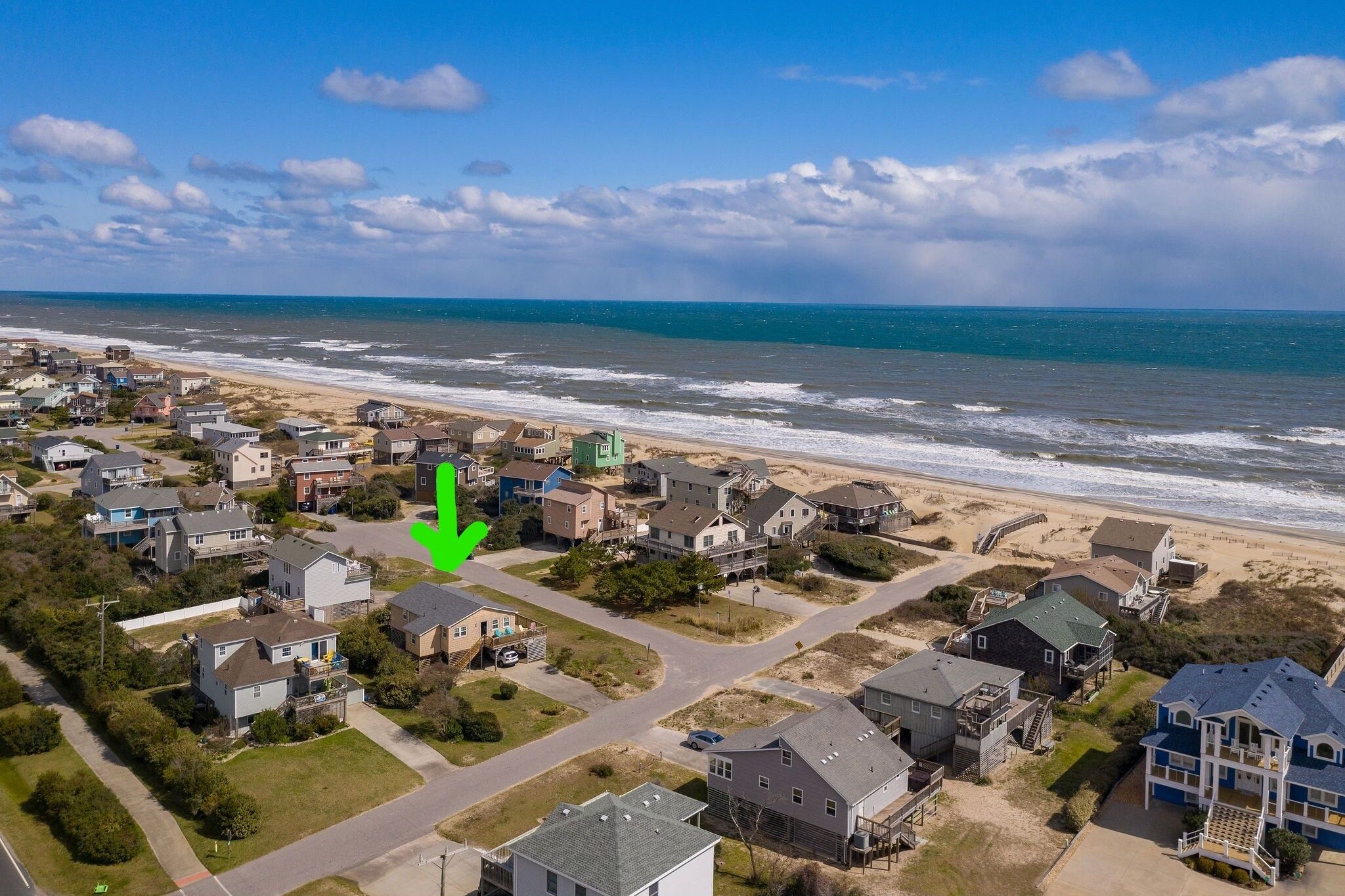 An aerial view of a coastal residential area with houses, roads, and a beach.