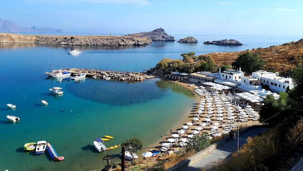 A coastal area with boats docked, a beach with umbrellas, and buildings with white walls.