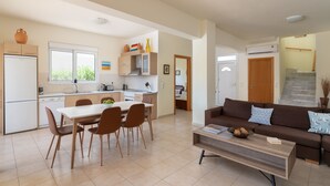 A modern kitchen with a dining area, a living room with a sofa and coffee table, and a staircase leading to another level.
