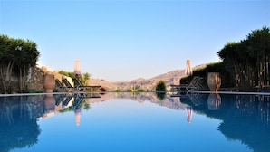 A serene pool area with lounge chairs and umbrellas, surrounded by lush greenery and a clear view of distant hills.