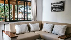 Un canapé beige agrémenté de quatre coussins à rayures, une table basse en bois ornée d’une décoration représentant un poisson aux couleurs vives, et un tableau représentant un paysage en noir et blanc accroché au mur.