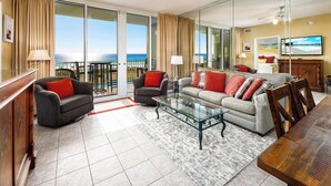 A spacious living room with a large glass sliding door leading to a balcony, a wooden dining table, and a comfortable seating area with sofas and armchairs.
